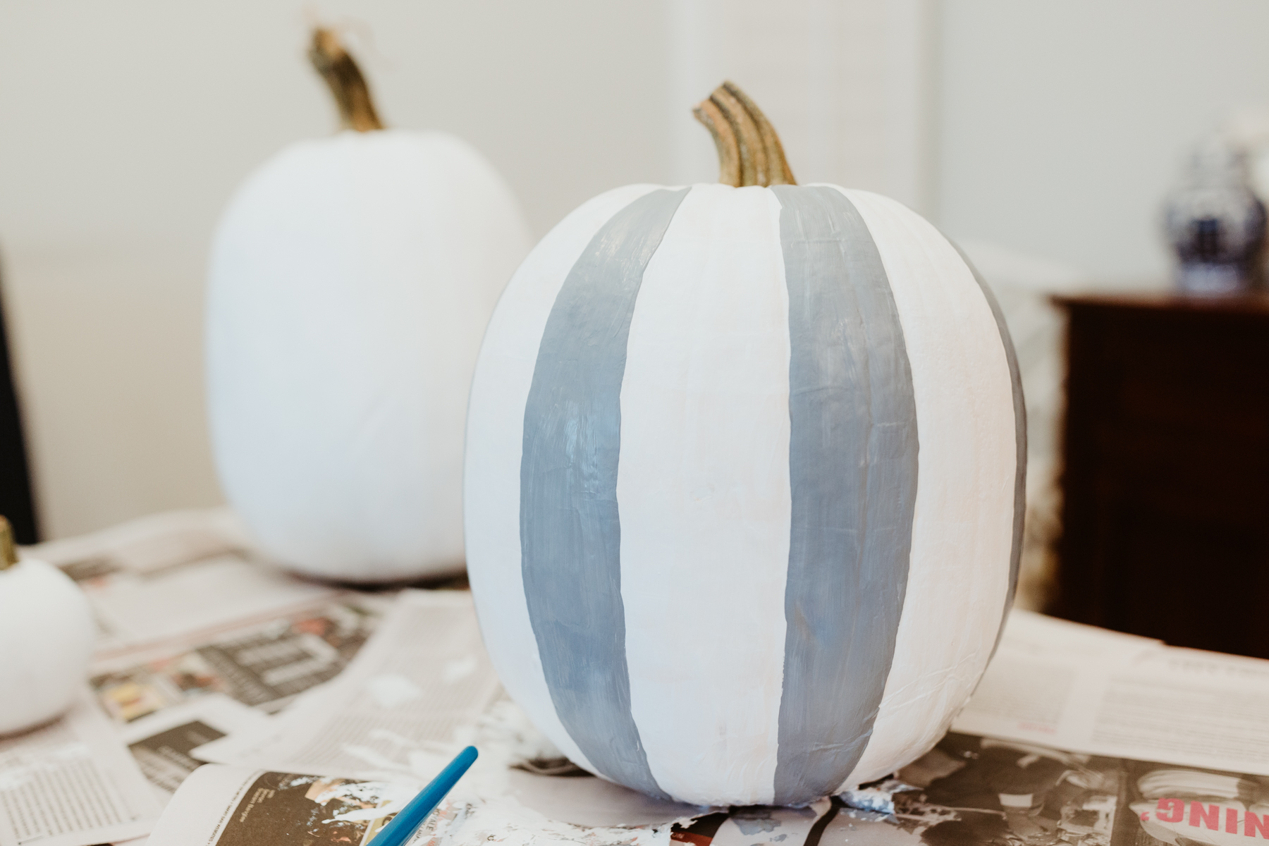 Buffalo plaid pumpkin: On a paper plate, mix the white and black paint to create your desired shade of gray. Then paint vertical stripes following the natural lines of the pumpkin. These lines aren't spaced out perfectly, so don't think of them as borders. Simply use them as guides!