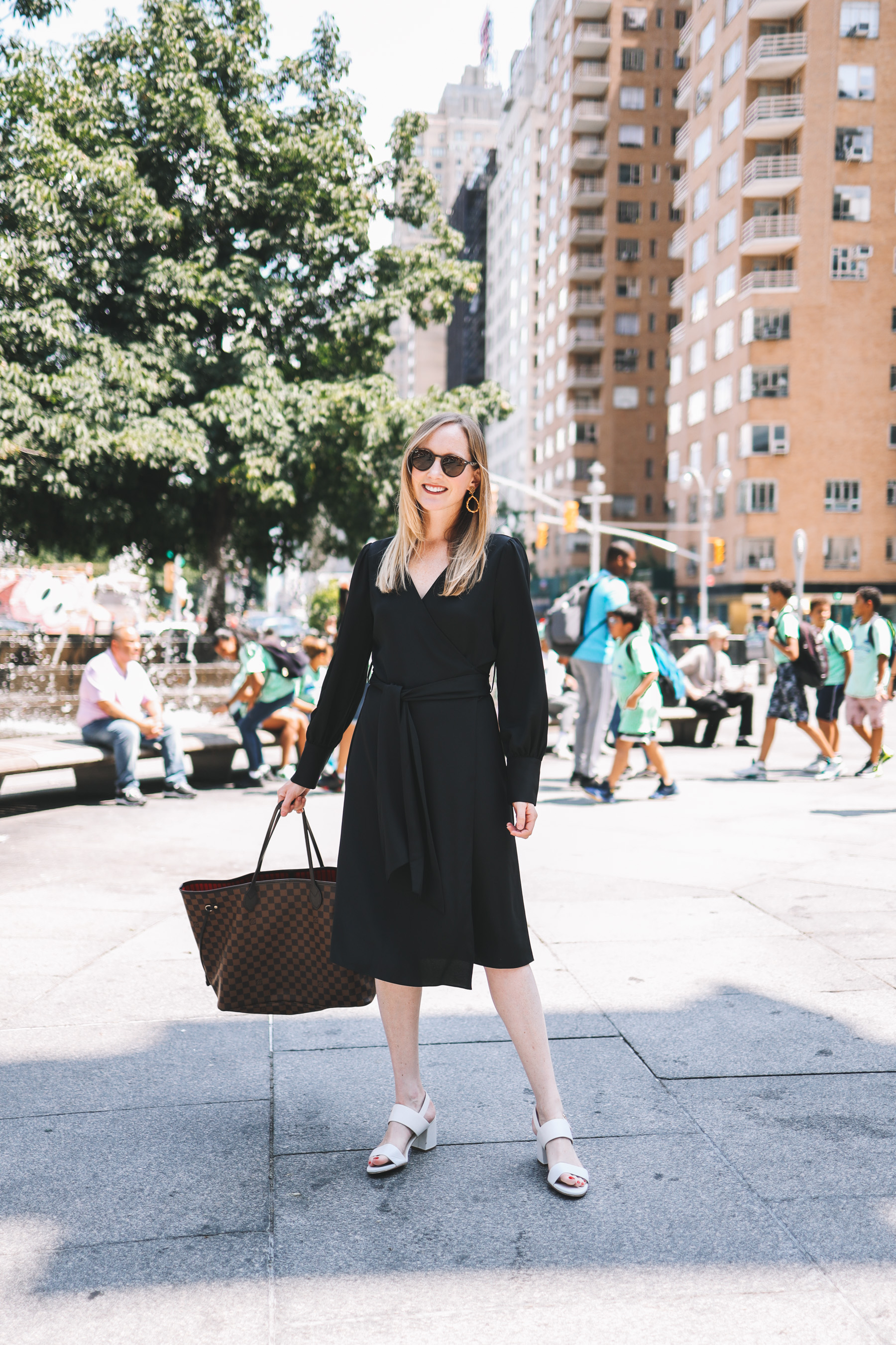 Kelly in a black wrap dress holding a Louis Vuitton purse