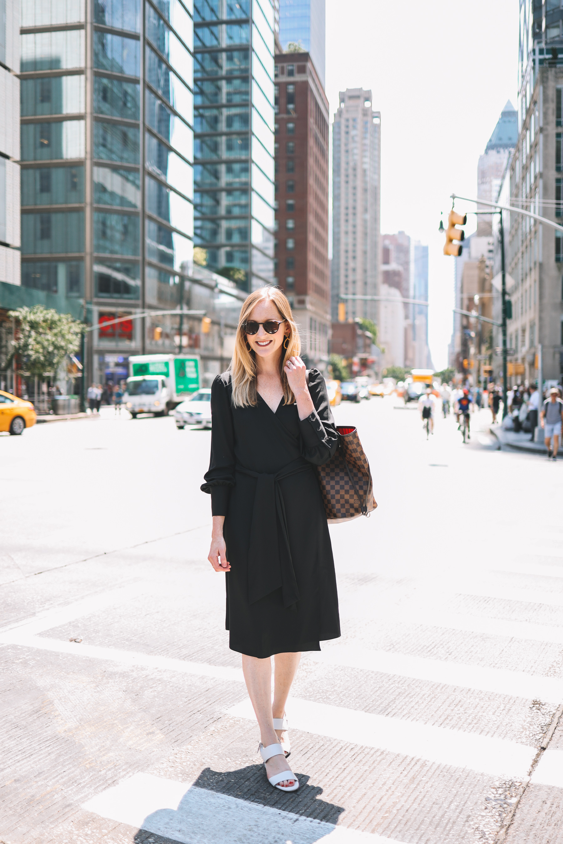 Kelly smiling in a black wrap dress with a New York City street in the background