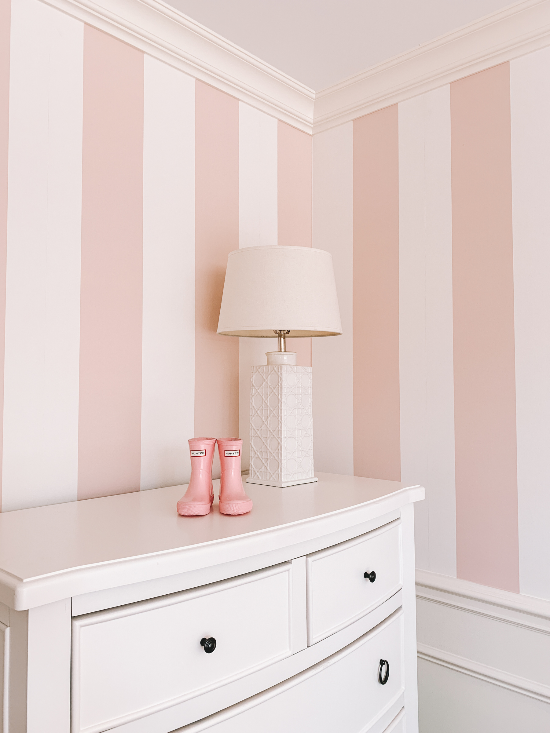 Pink baby Hunter boots are displayed on top of white dressed with pink-stripped wallpaper in the backdrop