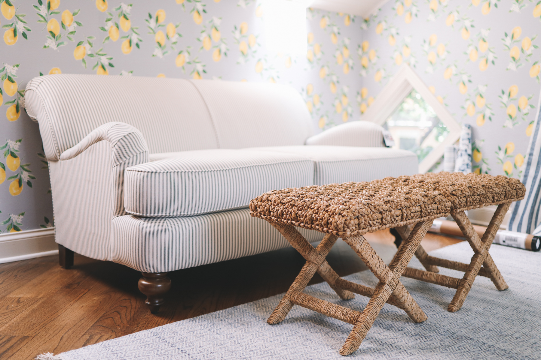 A custom striped loveseat for under $600 is next to a woven coffee table and lemon wallpaper in Kelly Larkin's living room