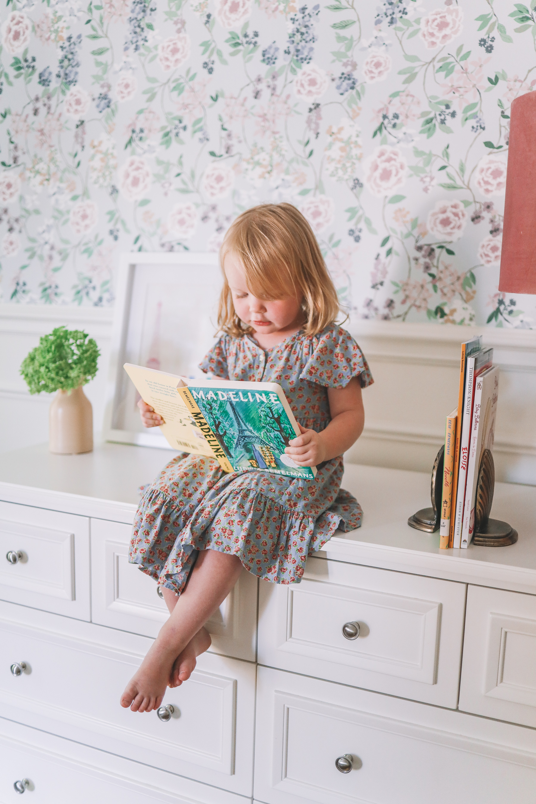 flower home of this little girl who is reading on a dresser