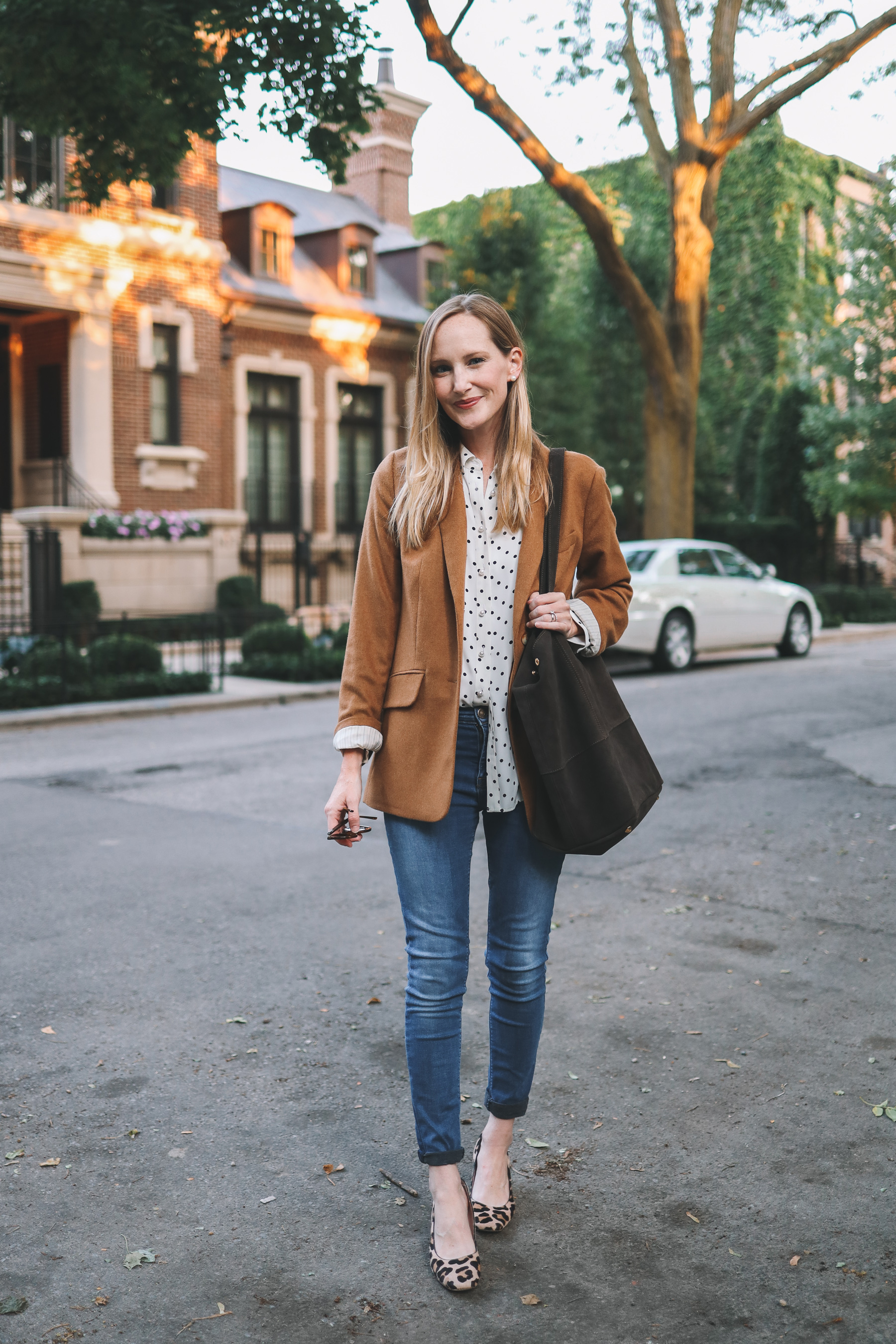 a woman in a brown jacket and a polka dot shirt wearing a leather tote bag